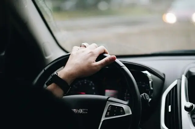 Eine Frau in schwarzer Kleidung am Steuer eines Fahrzeugs.